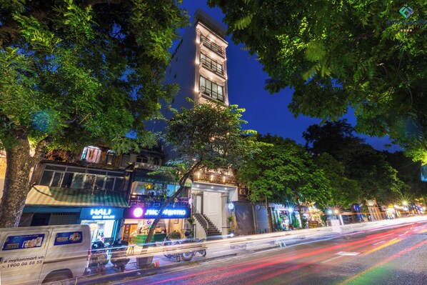 Un edificio de varios pisos con balcones, rodeado de árboles e iluminado por farolas.