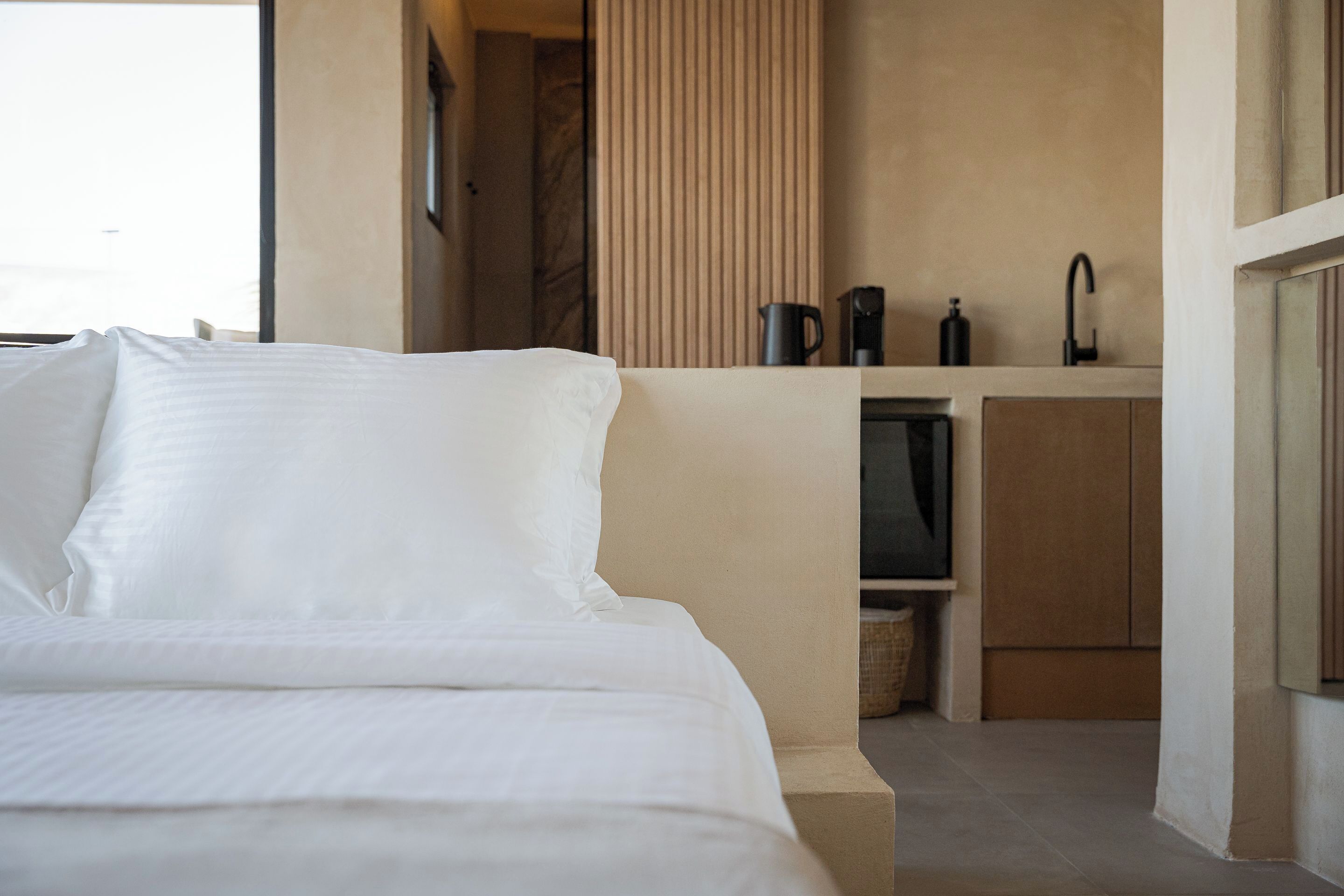 Una habitación de hotel moderna con una cama, televisión integrada, una kitchenette pequeña y un ventanal.