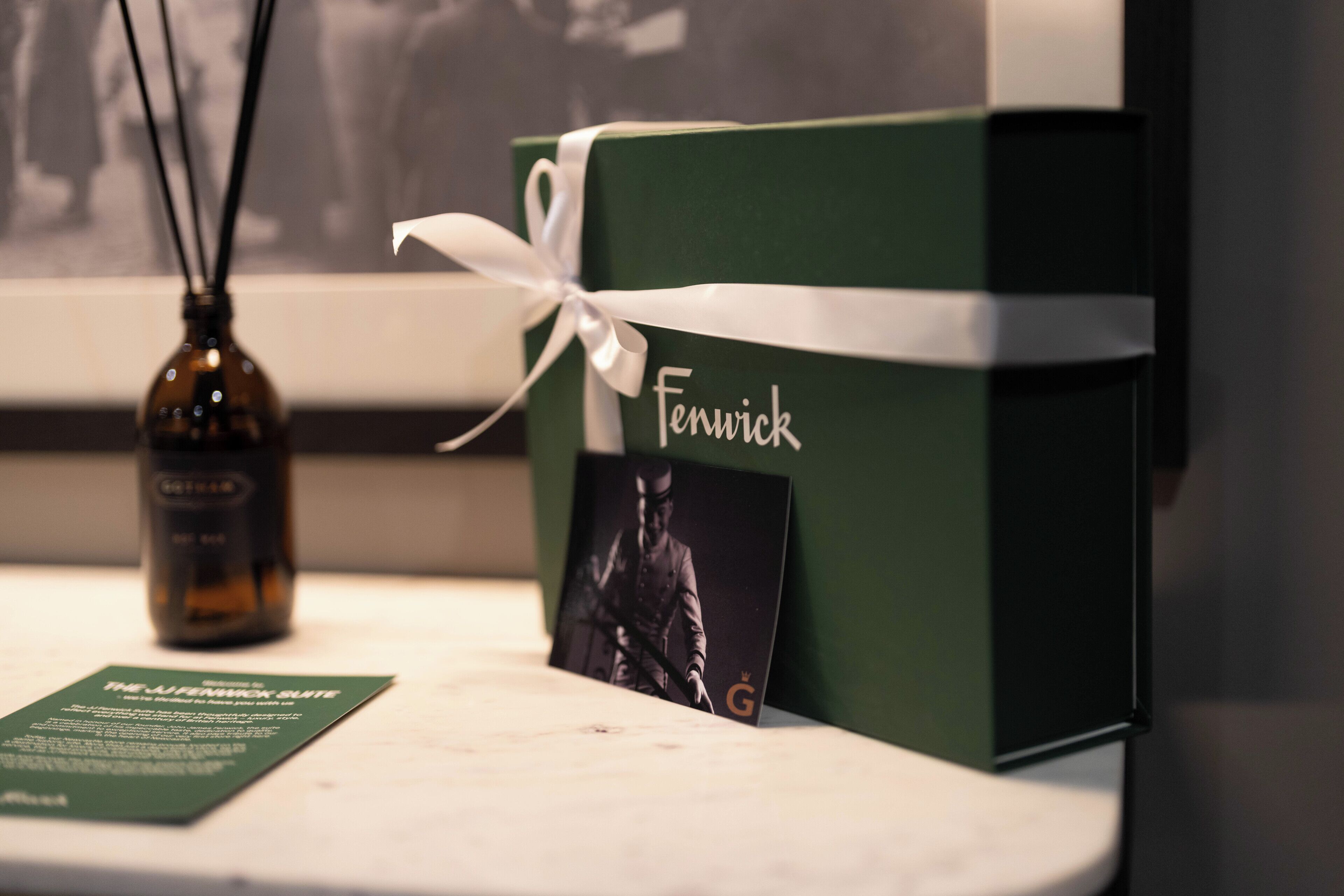 A green gift box with a white ribbon and a name tag, placed on a table with a bottle and a menu.