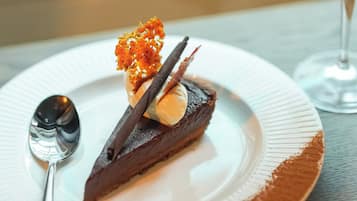 Un postre en un plato con una cuchara a un lado, y una copa de vino tinto al fondo.