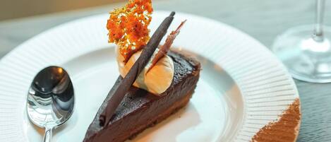 A dessert on a plate with a spoon beside it, and a glass of red wine in the background.