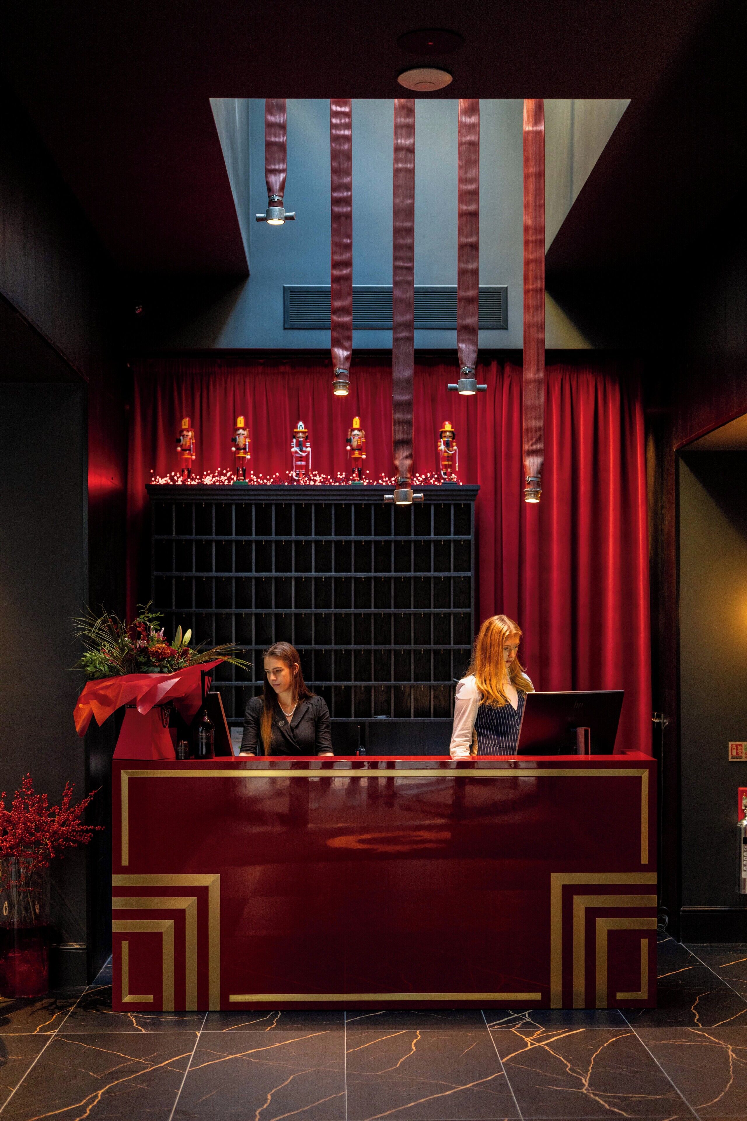 A reception desk with a red and gold design, a potted plant, and a decorative window with lights.