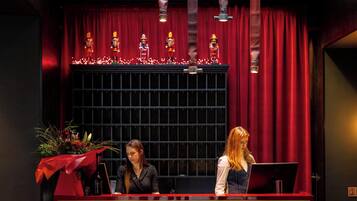 A reception desk with a red and gold design, a potted plant, and a decorative window with lights.