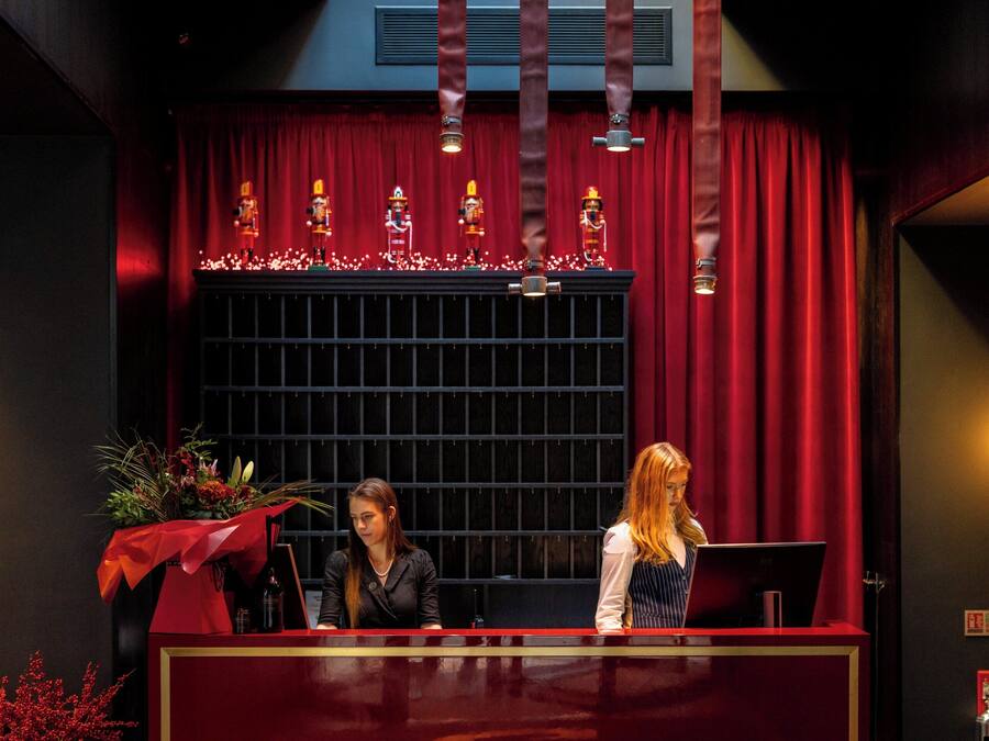 A reception desk with a red and gold design, a potted plant, and a decorative window with lights.