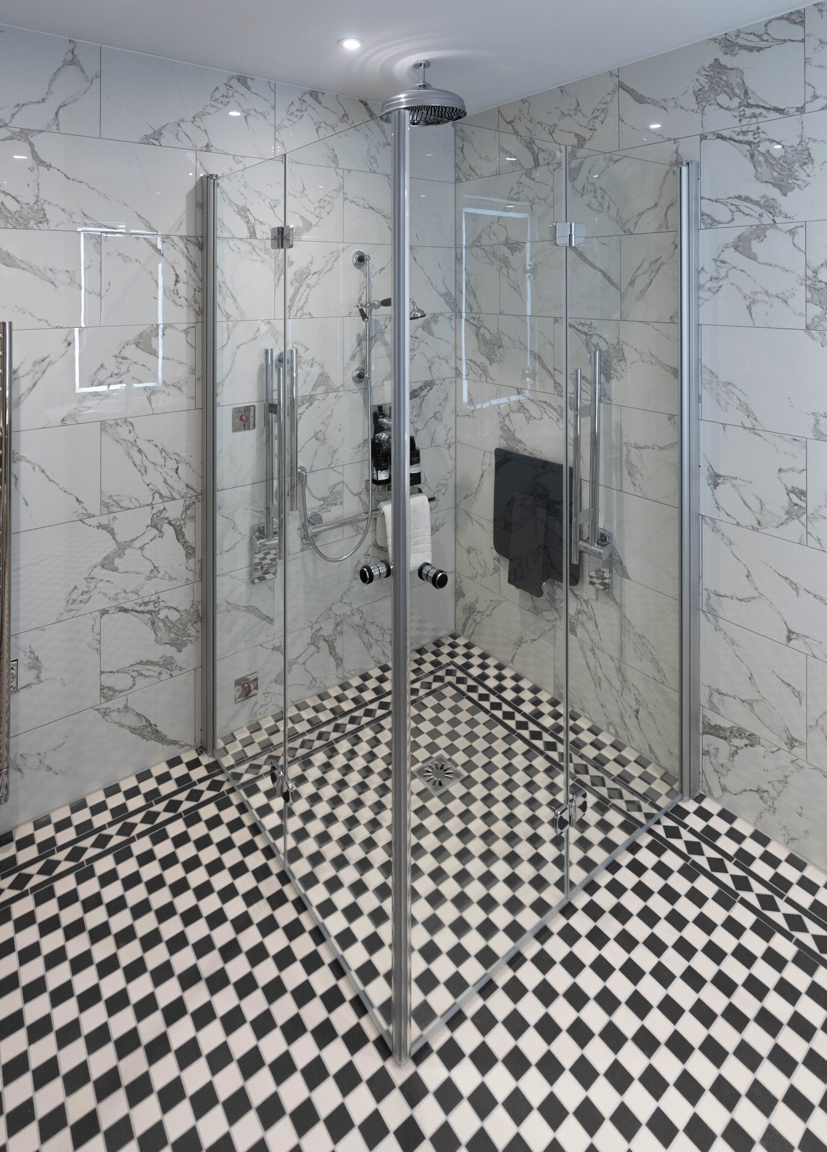 A modern bathroom with a glass-enclosed shower, marble walls, and a checkered floor.