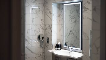 A bathroom with a marble floor, a white sink, a large mirror, and a shower.
