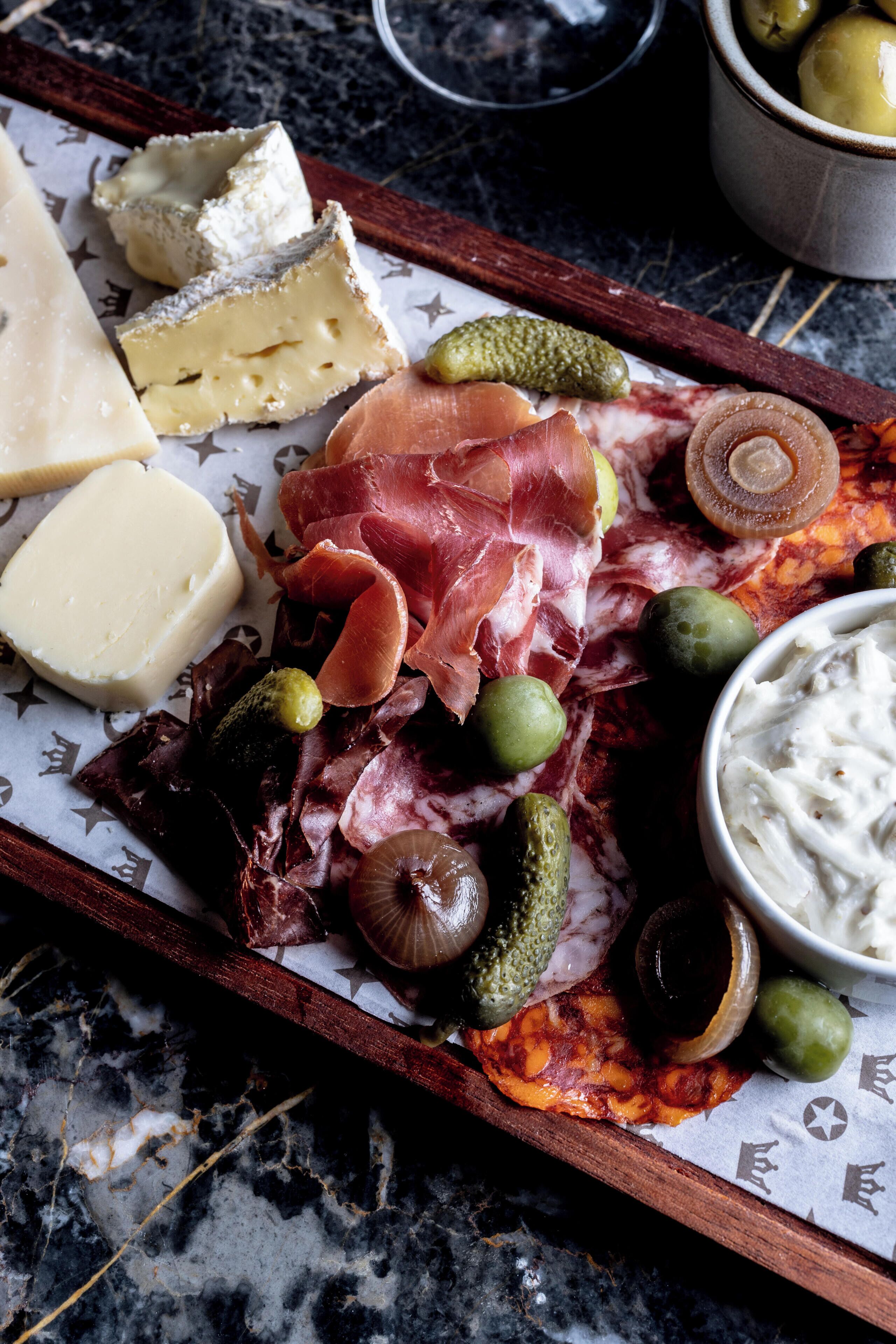 A charcuterie board with cheese, cured meats, olives, and pickles.