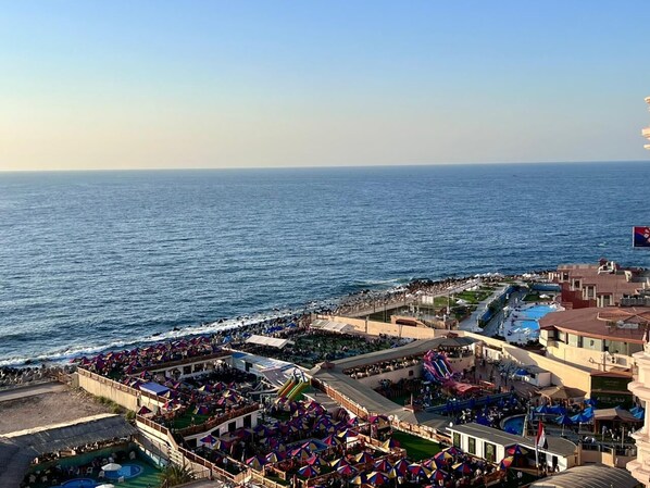 Ein Küstenort mit Strandabschnitt, Pool und Promenade mit Sonnenschirmen.