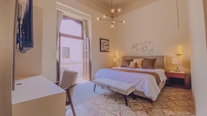 Ein Hotelzimmer mit Bett, Nachttischen, einem Schreibtisch und einem Stuhl. Es gibt einen Balkon mit Blick auf Gebäude.