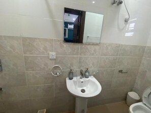 A bathroom with a white sink, two faucets, a mirror above the sink, and a toilet to the right. - Rove Luxury Hotel and Suites (Mgbakwu)
