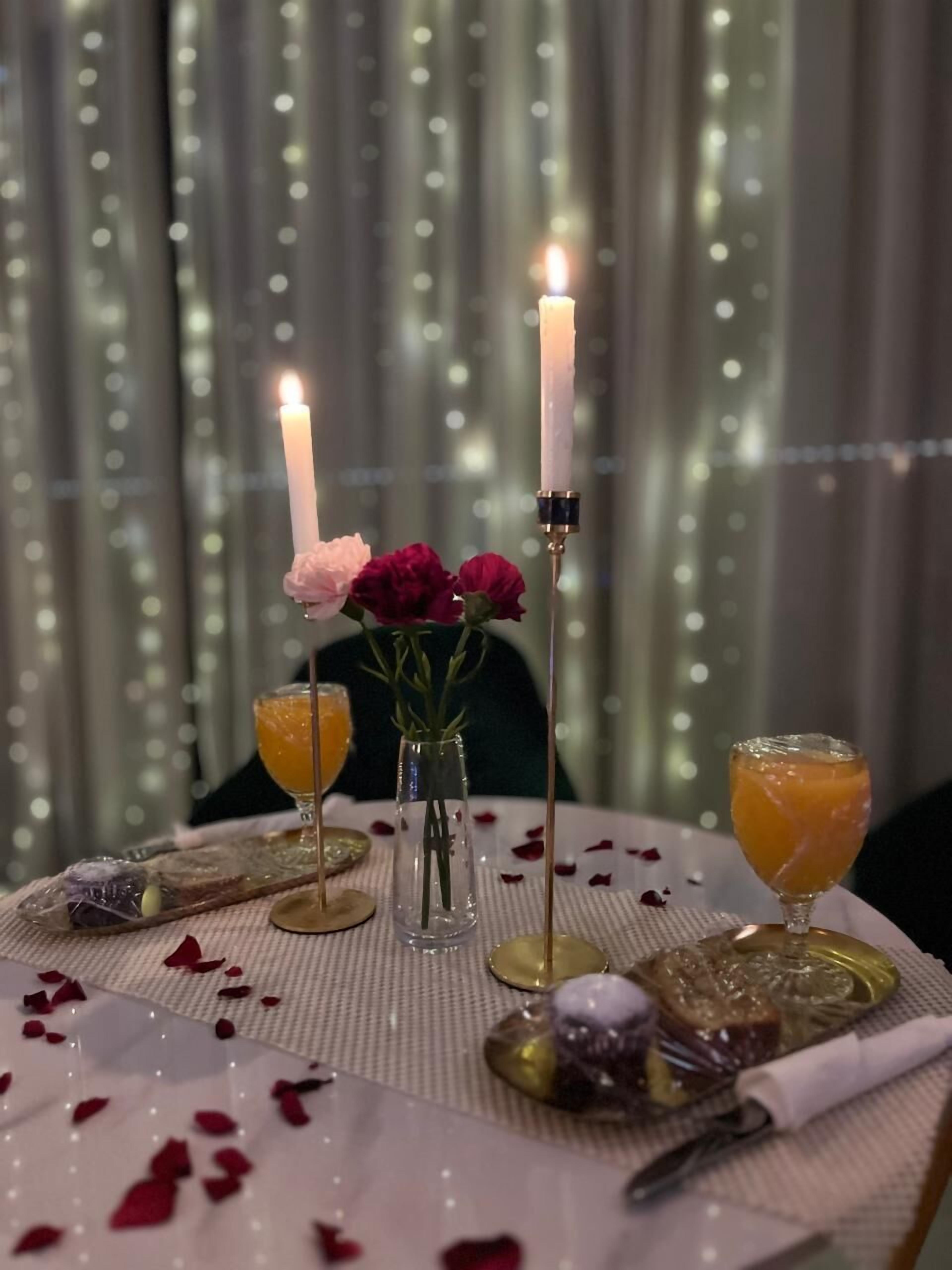 A table set with candles, a vase of flowers, and two glasses of orange juice.
