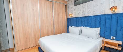 Une chambre à coucher avec un grand lit, une armoire en bois, une tête de lit bleue et deux lampes fixées au mur.