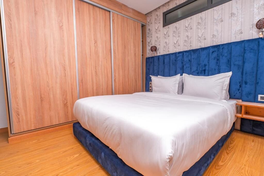 Een slaapkamer met een groot bed, een houten garderobe en een blauw hoofdeinde.