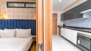 A modern hotel room with a large bed, a wooden door, and a kitchen area with a stove and cabinets. - MAARIF ELITE SUITES (Casablanca)