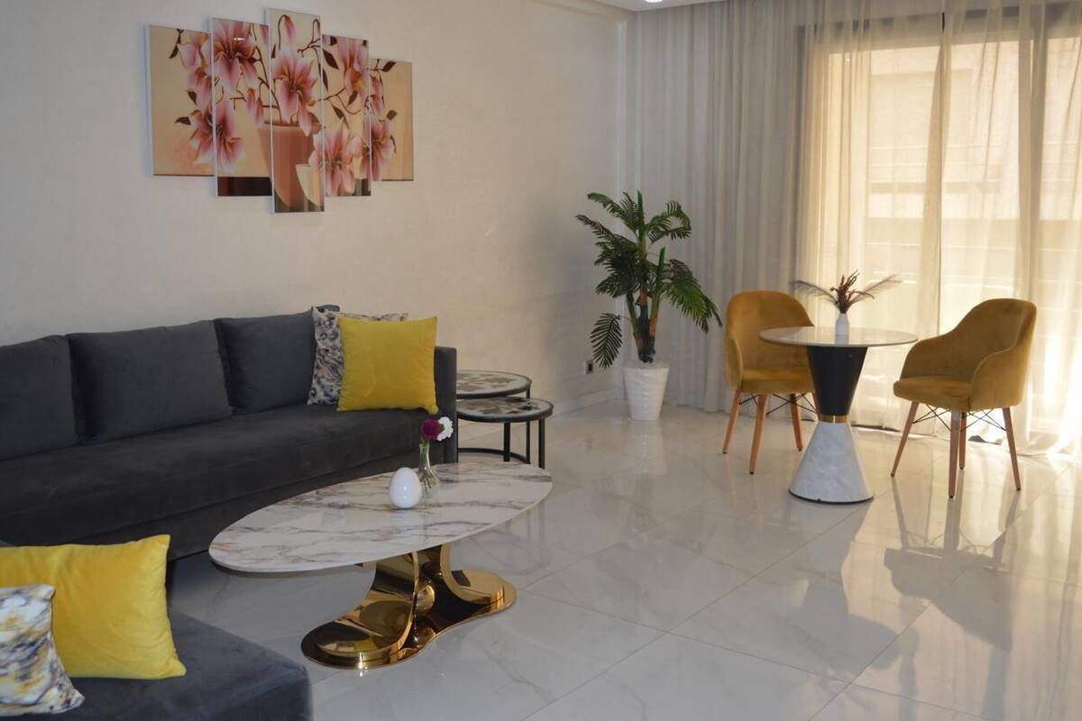 Un salon moderne avec un canapé gris foncé, des coussins jaunes, une table basse en marbre et une table de salle à manger ronde avec des chaises jaunes.