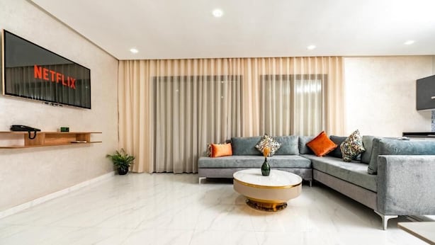 A modern living room with a sectional sofa, a round coffee table, and a mounted TV displaying 'NETFLIX'. - MAARIF ELITE SUITES (Casablanca)