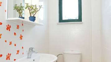Un baño con lavamanos blanco, inodoro y ventana con marco verde.
