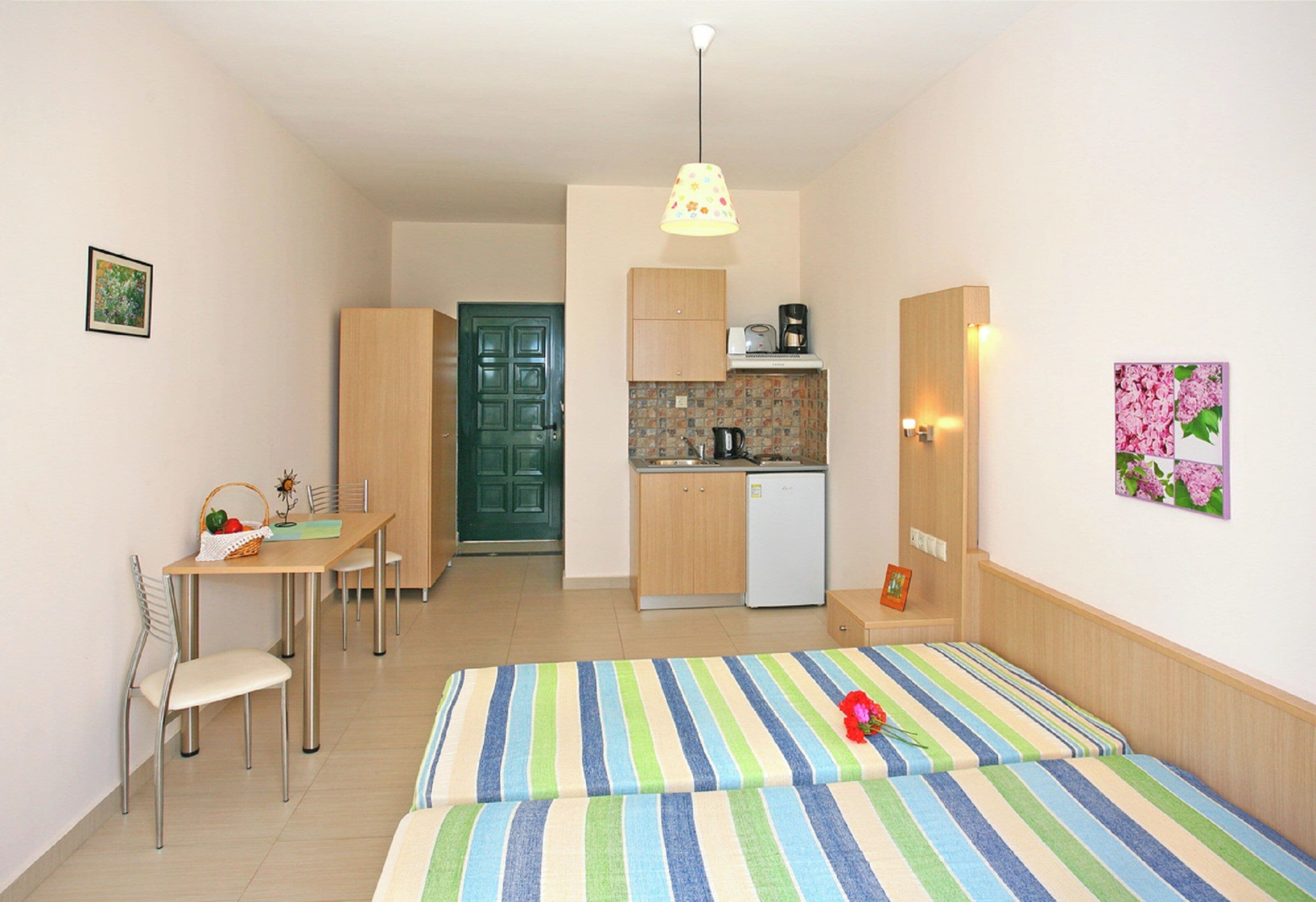 A compact room with a bed, a small dining table, chairs, a kitchenette, and a door.