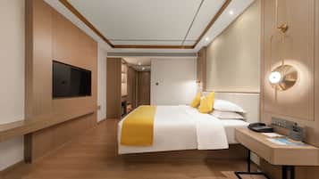 Ein modernes Hotelzimmer mit Bett, Nachttisch, Fernseher und Schreibtisch mit Lampe.