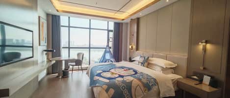 Ein modernes Hotelzimmer mit einem großen Bett, einem Schreibtisch und Blick auf eine Stadtlandschaft durch große Fenster.