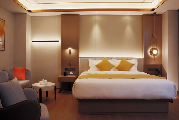 Una habitación de hotel moderna con una cama grande, un sofá, una mesita y una lámpara fijada a la pared.