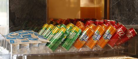 Un expositor de bebidas con varias latas y sobres, una cesta tejida y un recipiente metálico.