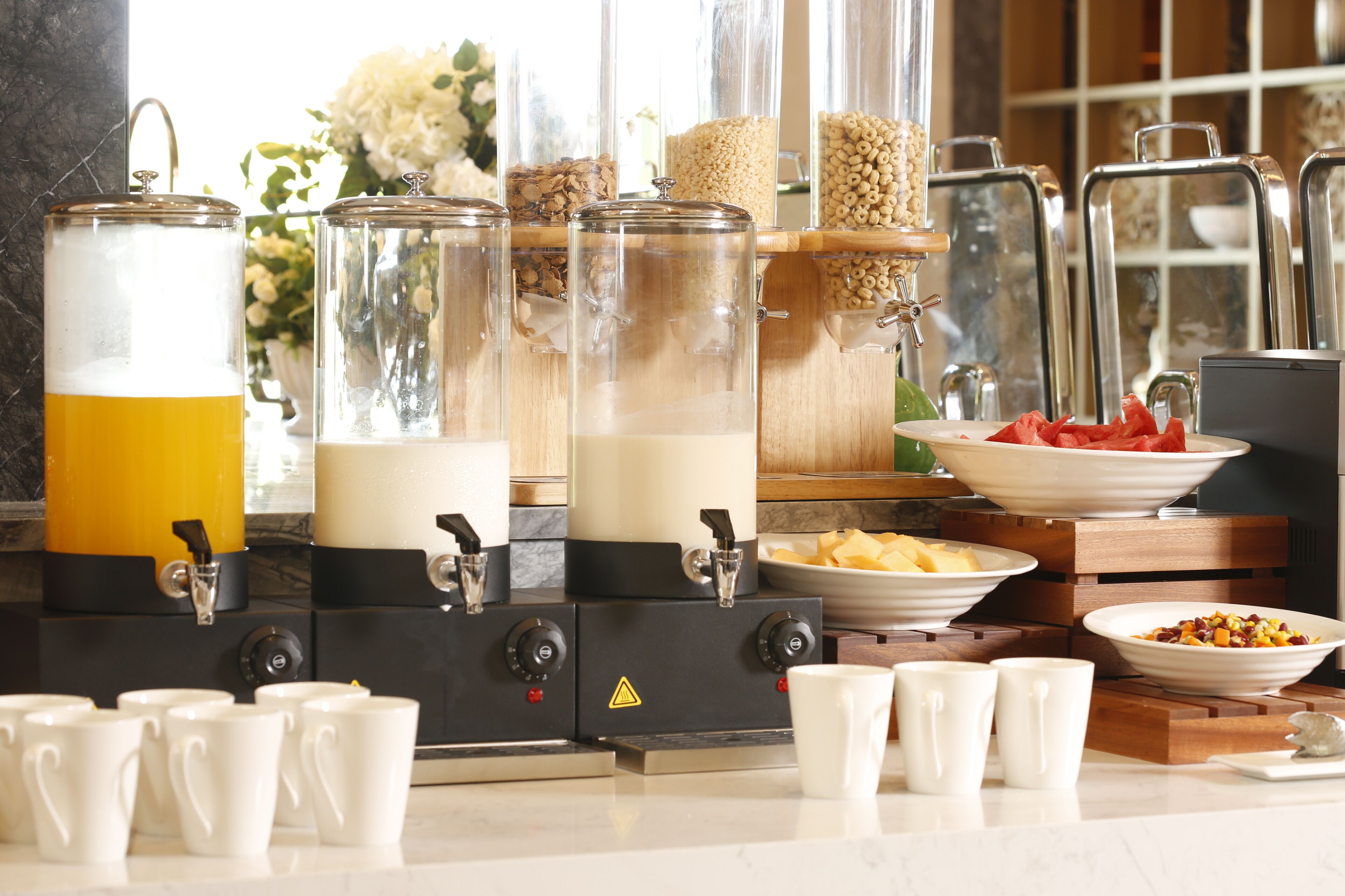 A breakfast buffet with various food options, a coffee station, and a flower arrangement.