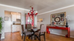 A dining area with a glass table, four chairs, a red desk, and a chandelier. - SeaCliff - Seaclusion - Oceanfront Luxury in Santa Barbara (Santa Barbara)