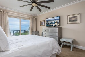Een slaapkamer met een groot bed, een plafondventilator, een televisie en uitzicht op zee.