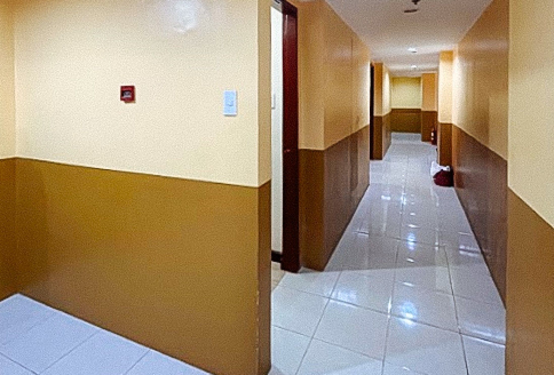 A hotel corridor with a tiled floor, beige walls, and a wooden door.