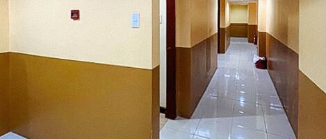 A hotel corridor with a tiled floor, beige walls, and a wooden door.