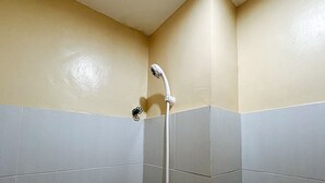 Canto de um banheiro com azulejos bege e cinzas, um chuveiro e um pequeno objeto decorativo na parede.