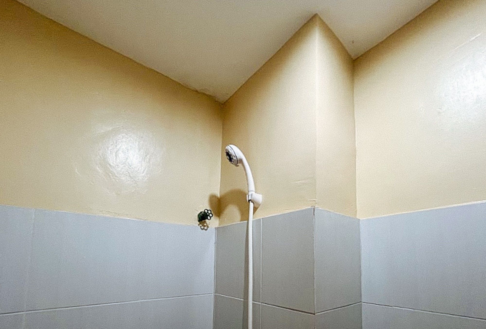 A corner of a bathroom with a shower area, tiled walls, and a corner sink.