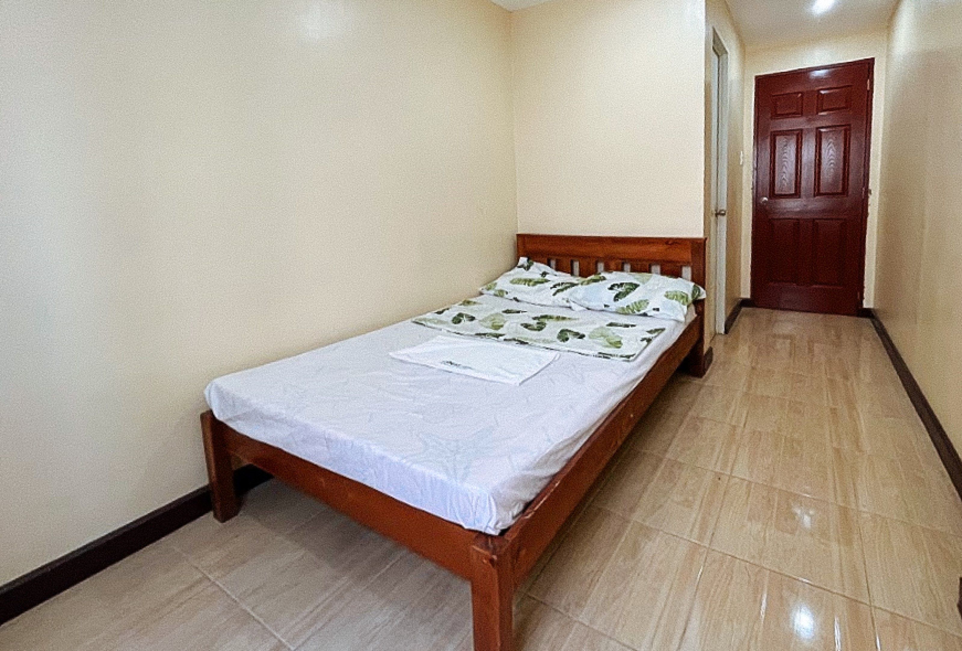 A small, single-bed room with a wooden headboard, a white bedspread, and a door in the background.
