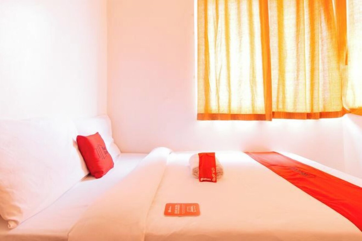 Ein Hotelzimmer mit einem Bett, einem roten Kopfkissen und einem Fenster mit Vorhängen.