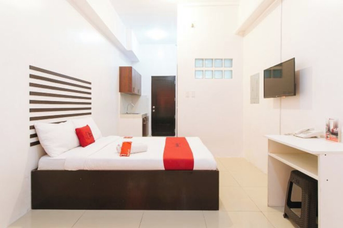 Una habitación de hotel moderna con una cama, un escritorio, un televisor y una pequeña kitchenette.