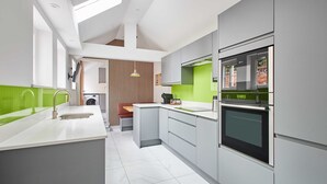 A modern kitchen with grey cabinets, a built-in oven, and a green accent wall. - Host Stay Damson Cottage (Pickering)