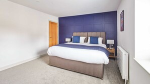 A bedroom with a large bed, a nightstand, a lamp, and a radiator. - Host Stay Damson Cottage (Pickering)