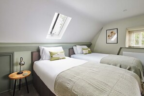 Habitación de hotel con dos camas, una mesita con lámpara, una ventana con persianas y un cuadro en la pared.