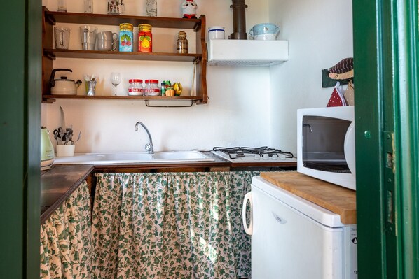 A compact kitchen with a sink, stove, and microwave. There are shelves above the sink holding various kitchen items.