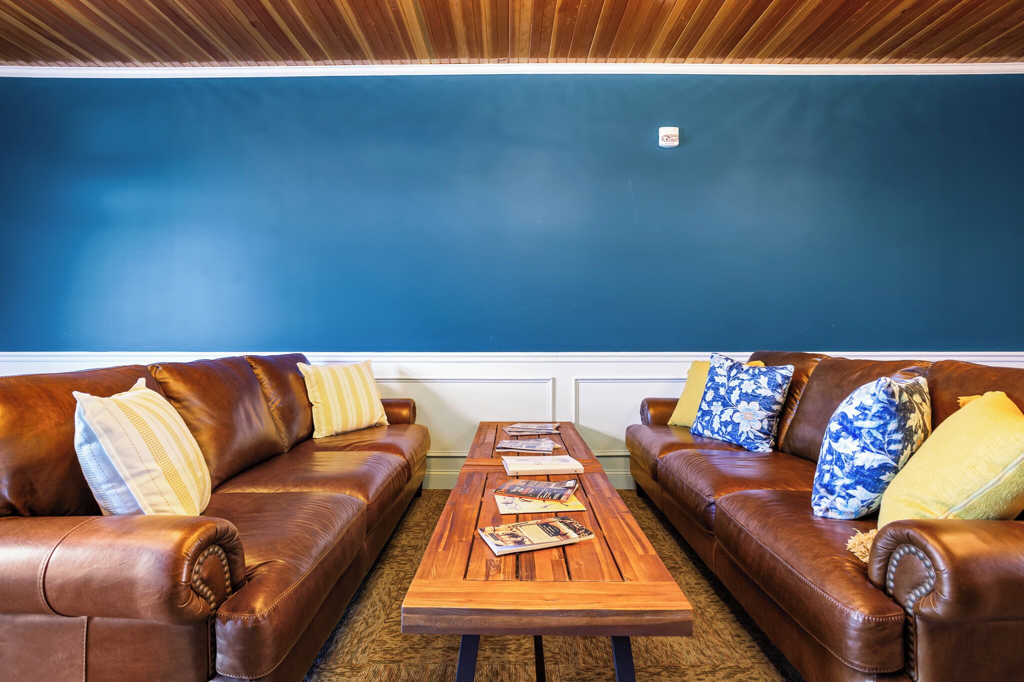 A room with two brown leather sofas, a wooden coffee table with magazines, and a blue wall.