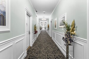 Un couloir d’hôtel avec un tapis à motifs, des murs blancs et des œuvres d’art encadrées.