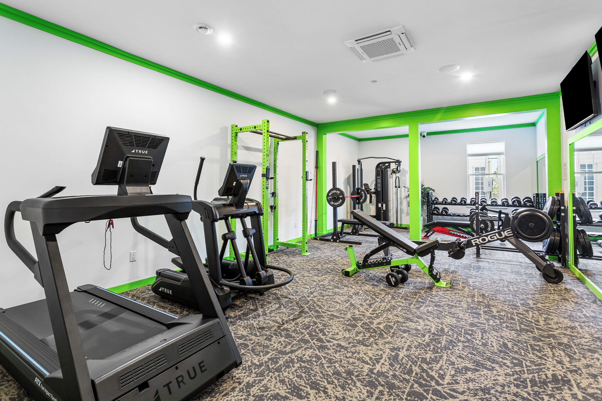 Une salle de sport équipée d’un tapis de course, d’un banc de musculation et de divers appareils d’exercice.