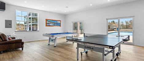 A spacious room with a ping pong table, a pool table, and a sofa.