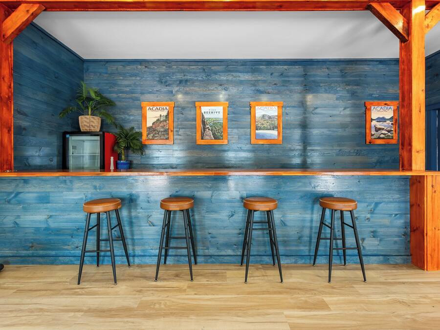 Angolo bar con pareti in legno, tre sgabelli e quadri appesi.