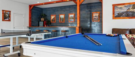 Ein Billardtisch mit blauer Spielvliesbahn, ein Tischtennisstisch und ein Barbereich mit Hockern.