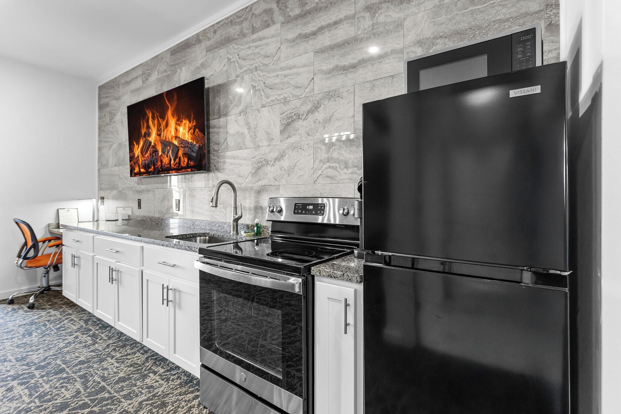 A modern kitchen with a stainless steel refrigerator, oven, and microwave, a marble backsplash, and a flat-screen TV mounted above the stove.