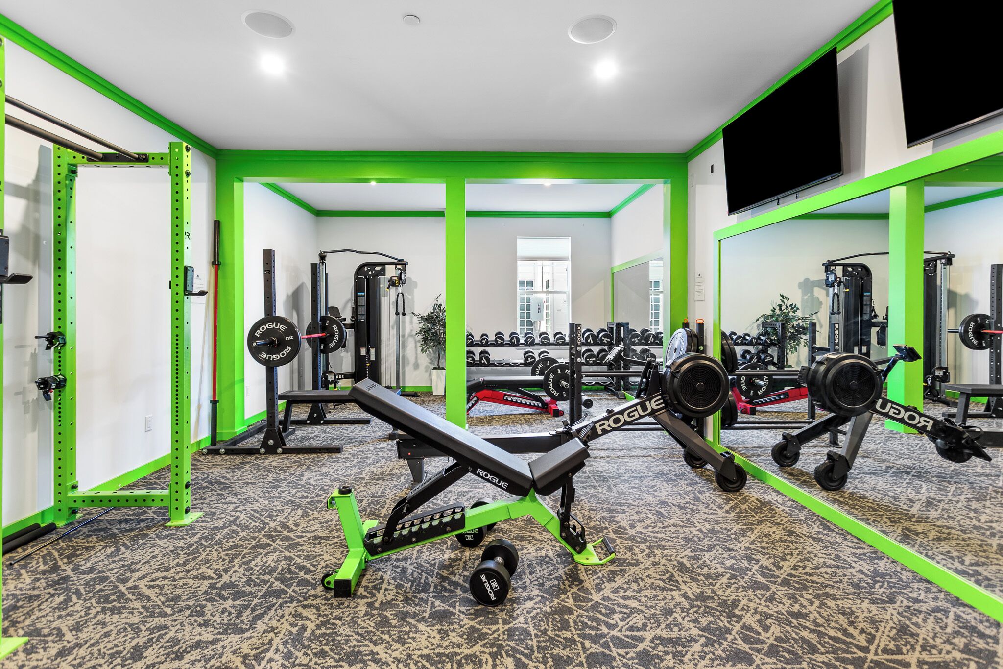 Une salle de sport équipée de matériel de musculation, agrémentée de touches de vert et dotée d’un grand miroir.