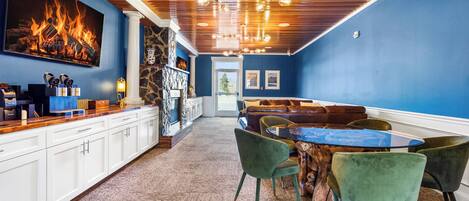 A room with a wooden ceiling, a fireplace, a dining area with a round table and chairs, and a view of the outdoors.