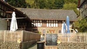 Un bâtiment traditionnel avec un toit en tuiles, une clôture en bois et un espace extérieur aménagé avec des parasols.